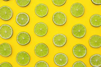 Photo of Slices of fresh juicy limes on yellow background, flat lay