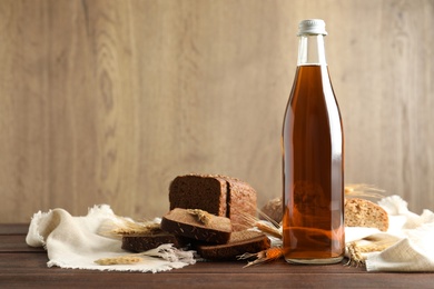 Photo of Bottle of delicious fresh kvass, spikelets and bread on wooden table