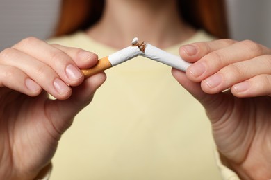 Stop smoking concept. Woman breaking cigarette on light gray background, closeup