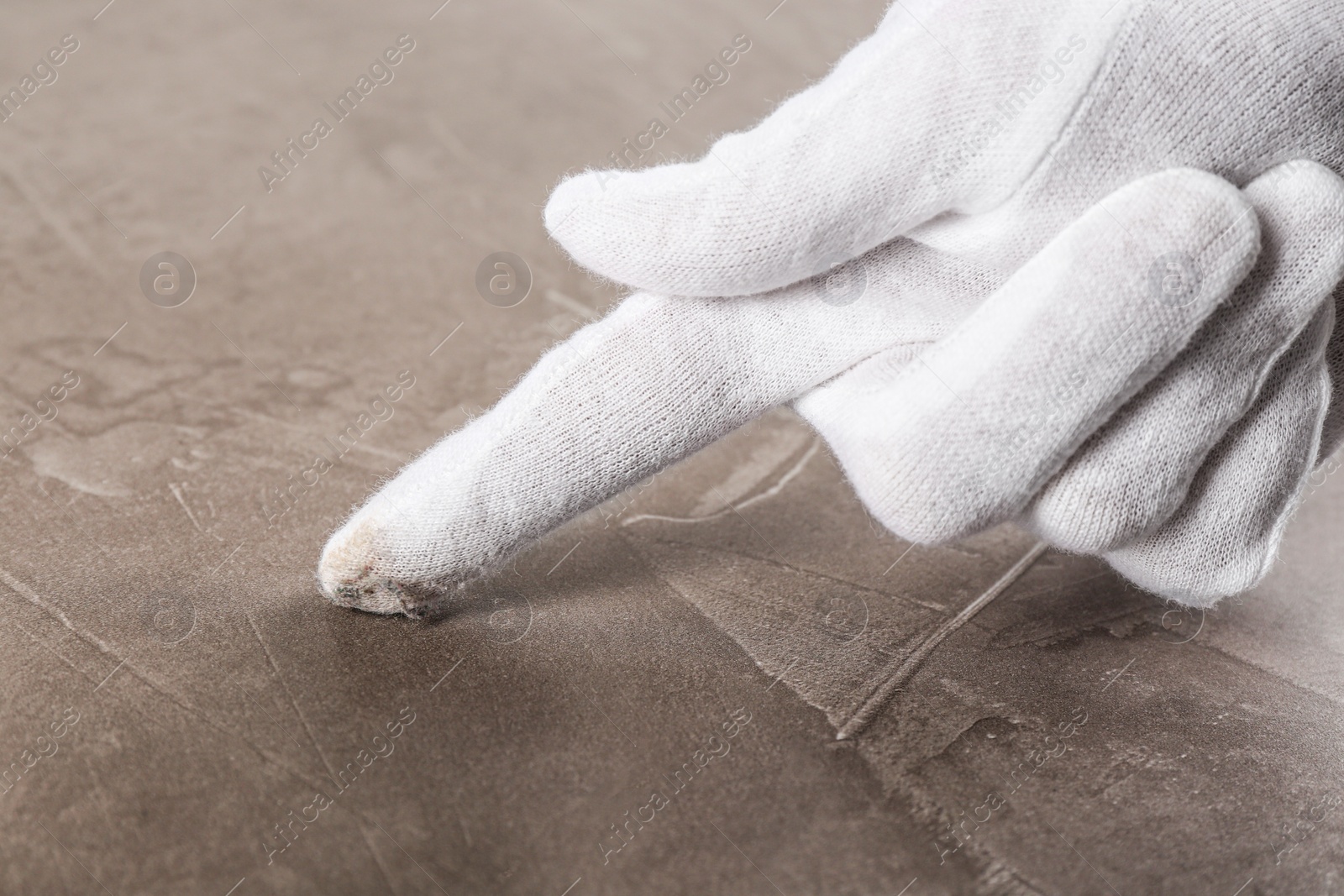 Photo of Person in white glove checking cleanliness of beige stone table, closeup