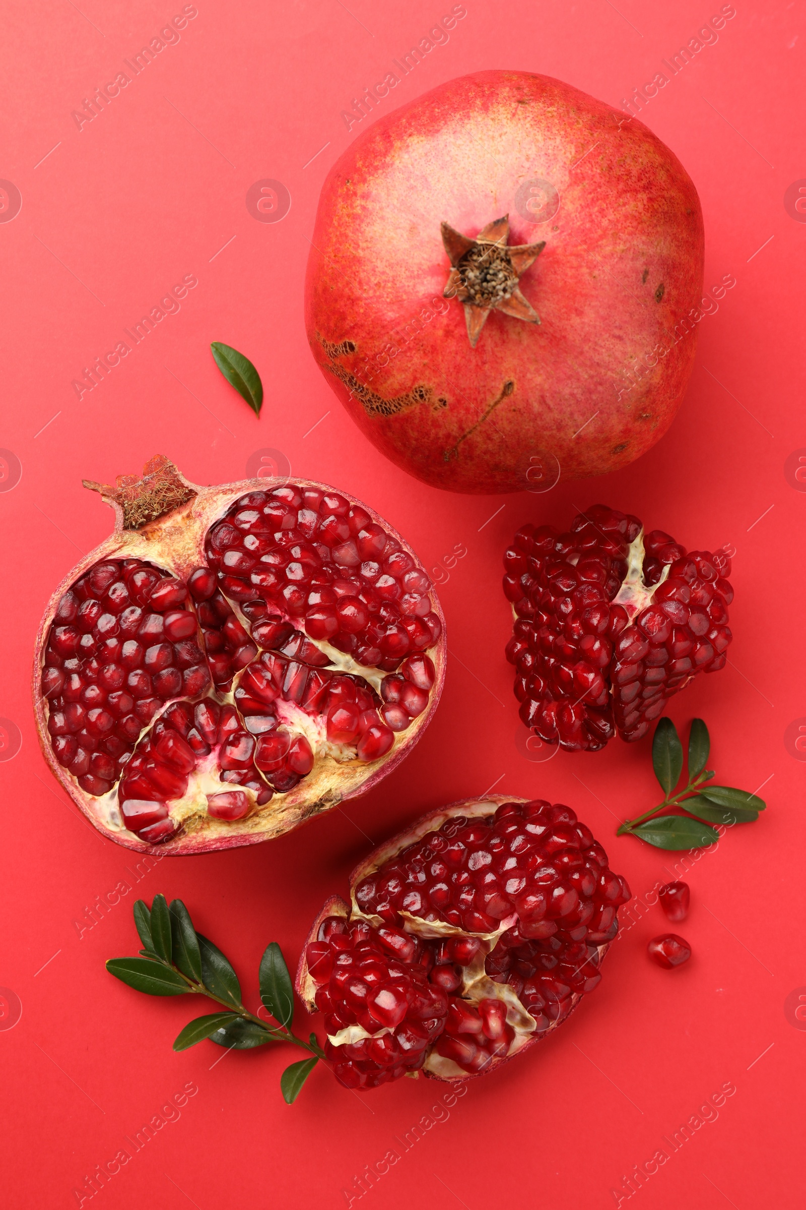 Photo of Fresh pomegranates and green leaves on red background, flat lay