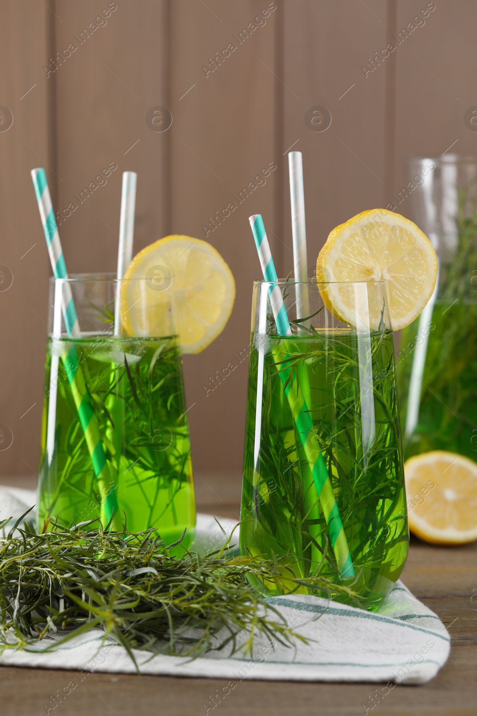 Photo of Glasses of refreshing tarragon drink with lemon slices on wooden table