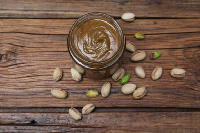 Tasty nut paste in jar and pistachios on wooden table, flat lay