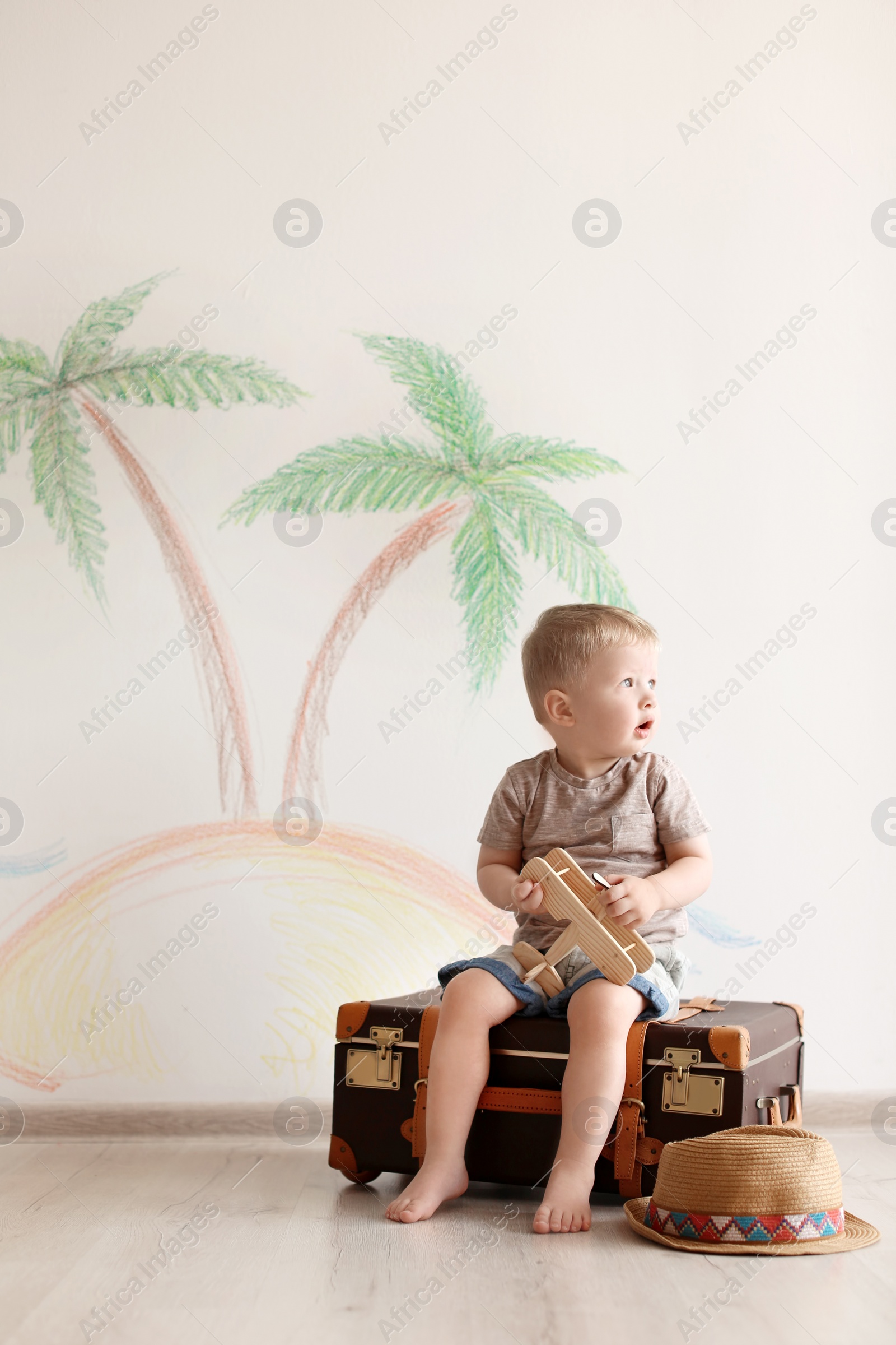 Photo of Adorable little child playing traveler with suitcase indoors