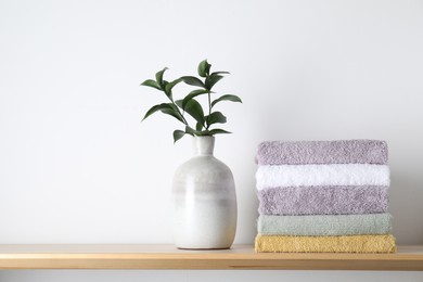 Stacked terry towels and green branches in vase on wooden shelf near white wall