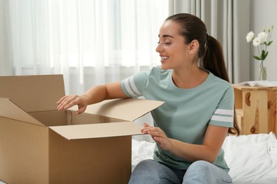 Happy young woman opening parcel on bed at home. Internet shopping