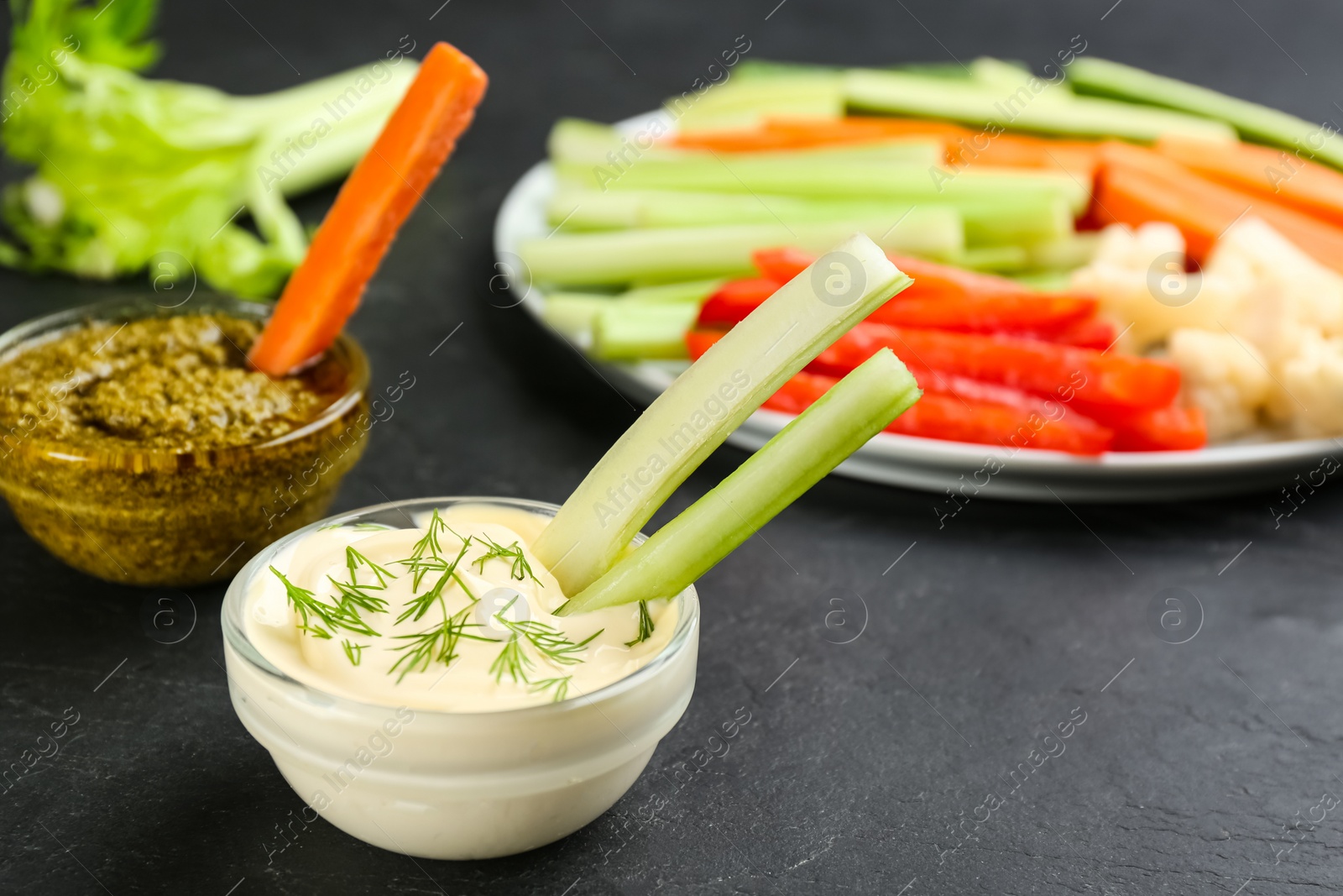 Photo of Celery sticks with dip sauce in glass bowl on black table