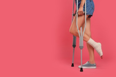 Photo of Young woman with injured leg using axillary crutches on pink background, closeup. space for text