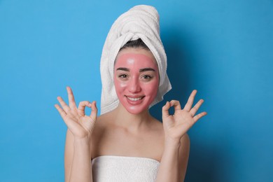 Woman with pomegranate face mask showing Ok on light blue background