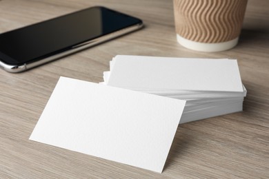 Photo of Blank business cards and smartphone on wooden table, closeup. Mockup for design