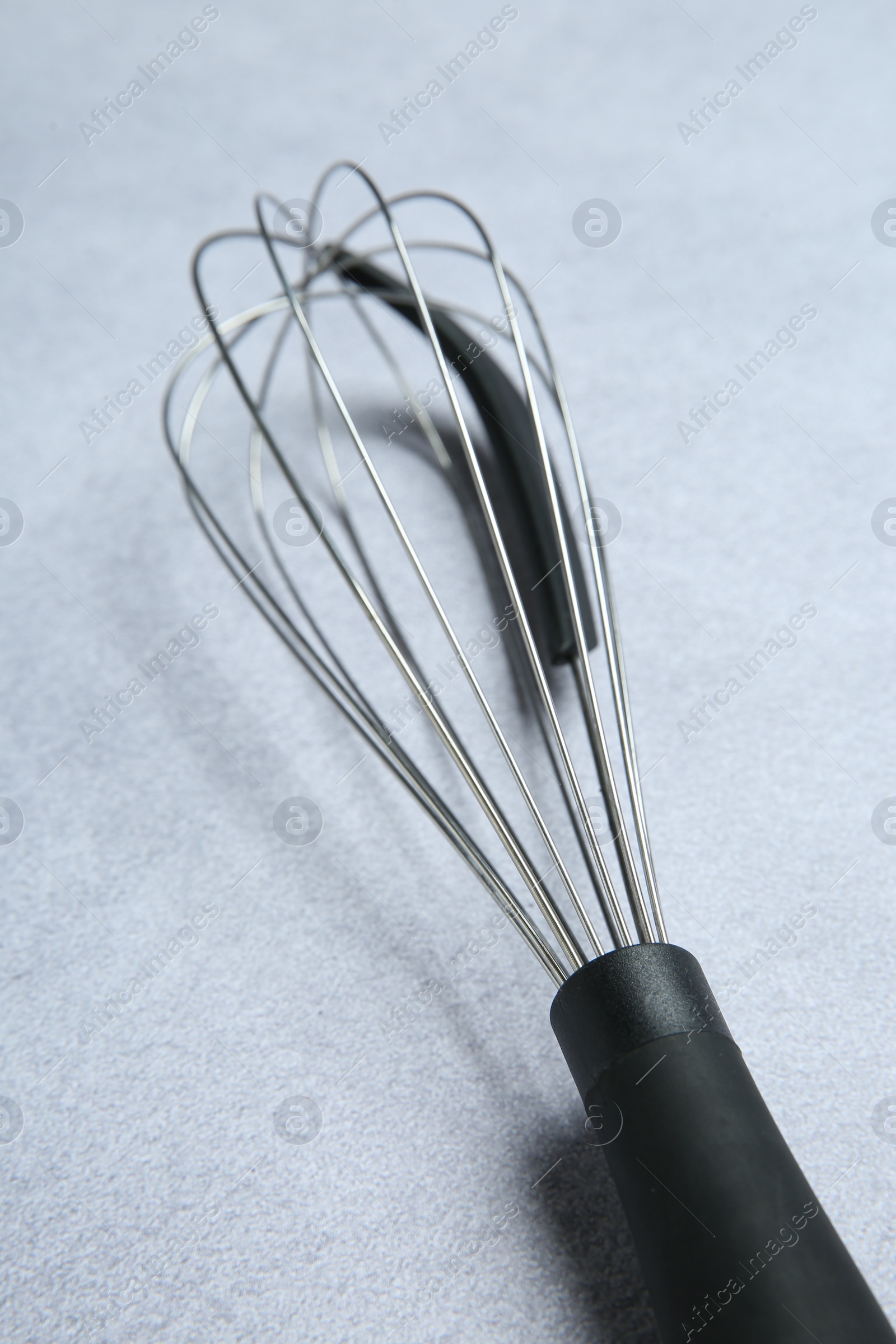 Photo of Metal whisk on gray table, closeup. Kitchen tool