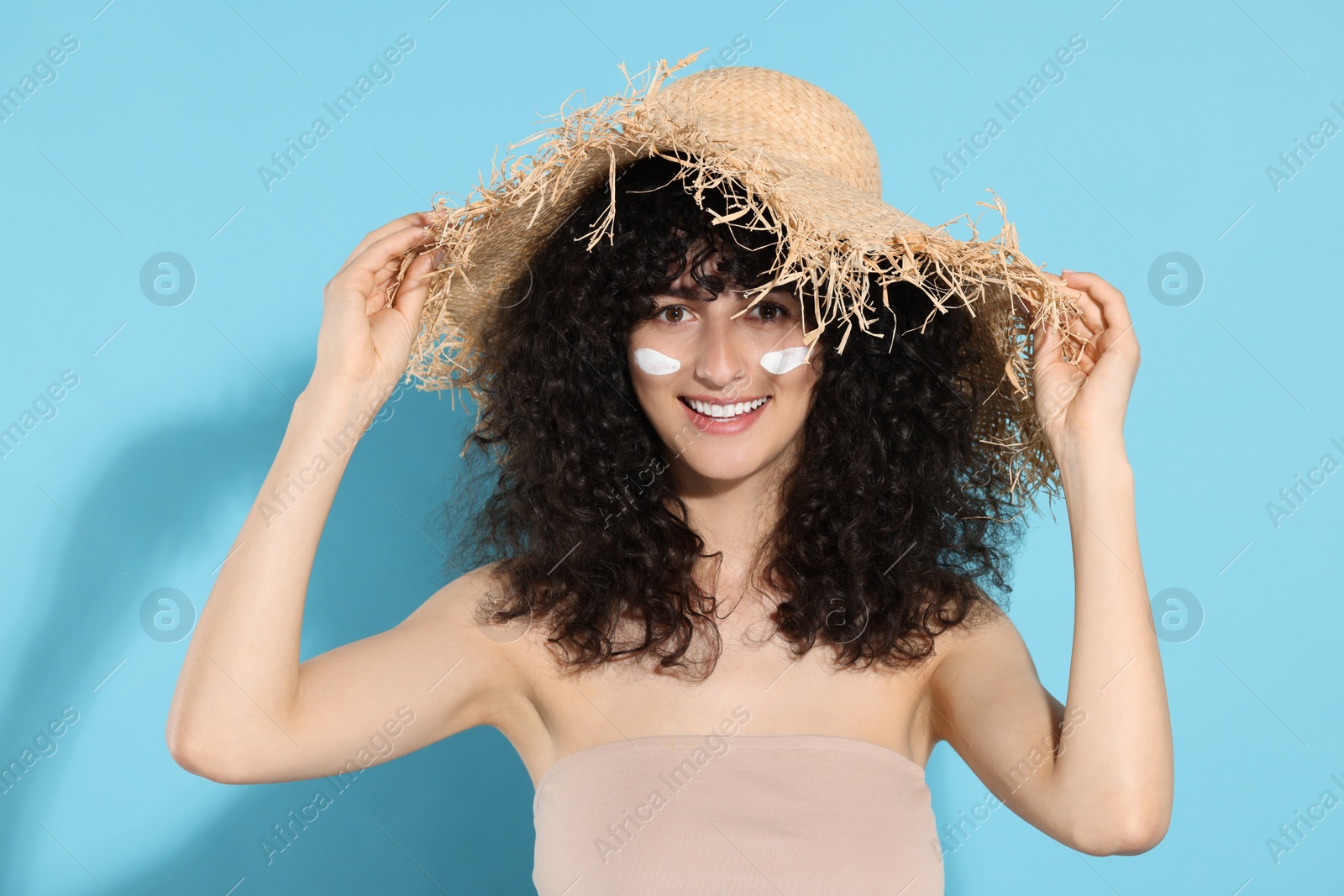 Photo of Beautiful young woman in straw hat with sun protection cream on her face against light blue background