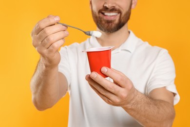 Photo of Man with delicious yogurt and spoon on yellow background, closeup