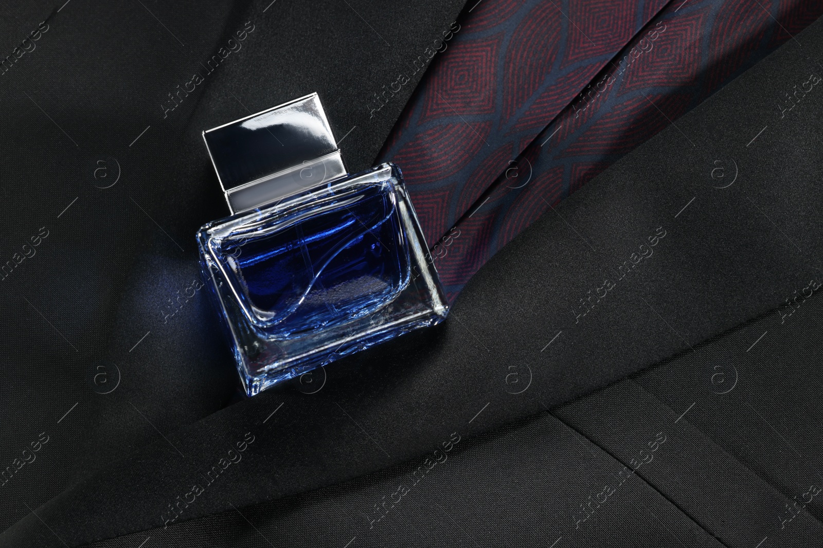 Photo of Luxury men's perfume in bottle on black jacket, top view. Space for text