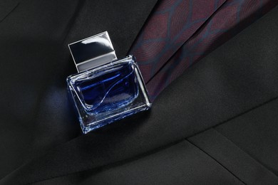 Luxury men's perfume in bottle on black jacket, top view. Space for text