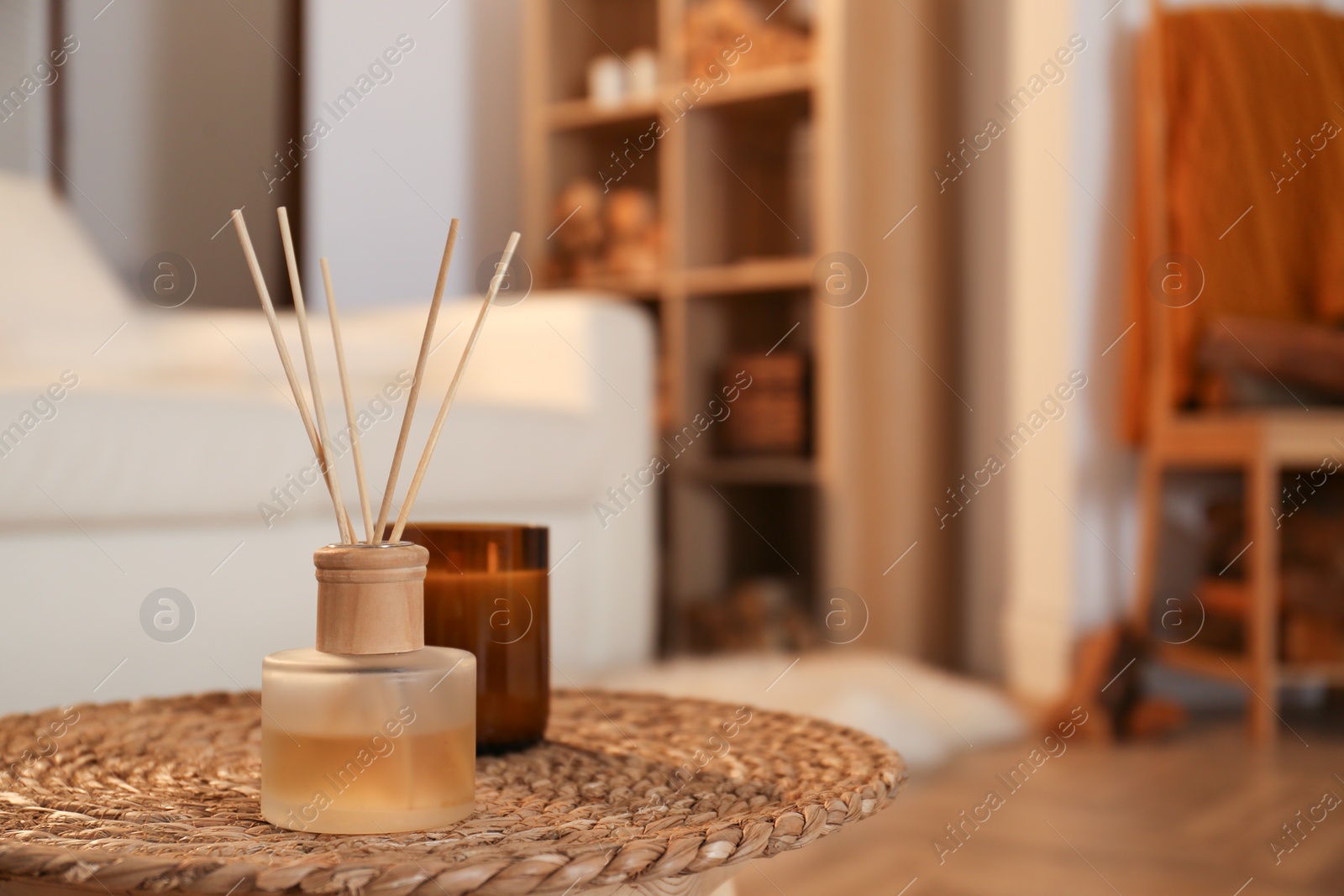 Photo of Aromatic reed air freshener and candle on wicker tray in room. Space for text
