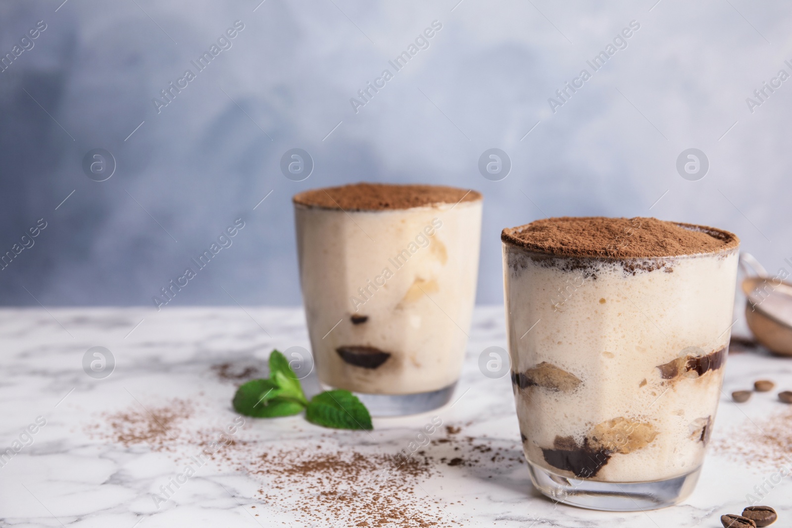 Photo of Two glasses of tiramisu cake on table against color background, space for text