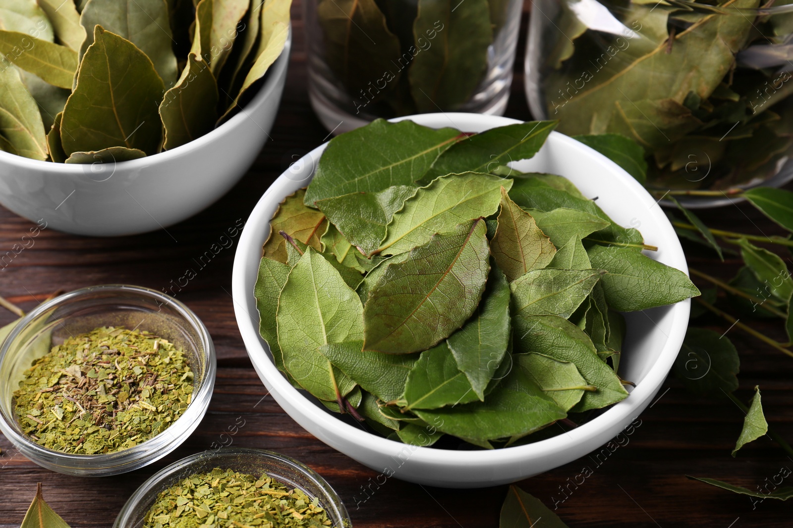 Photo of Bowls with ground, fresh and dry bay leaves on wooden table, view from above