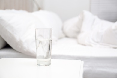 Glass of water on white nightstand in bedroom, space for text