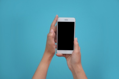 Photo of Young woman holding mobile phone with blank screen in hands on color background
