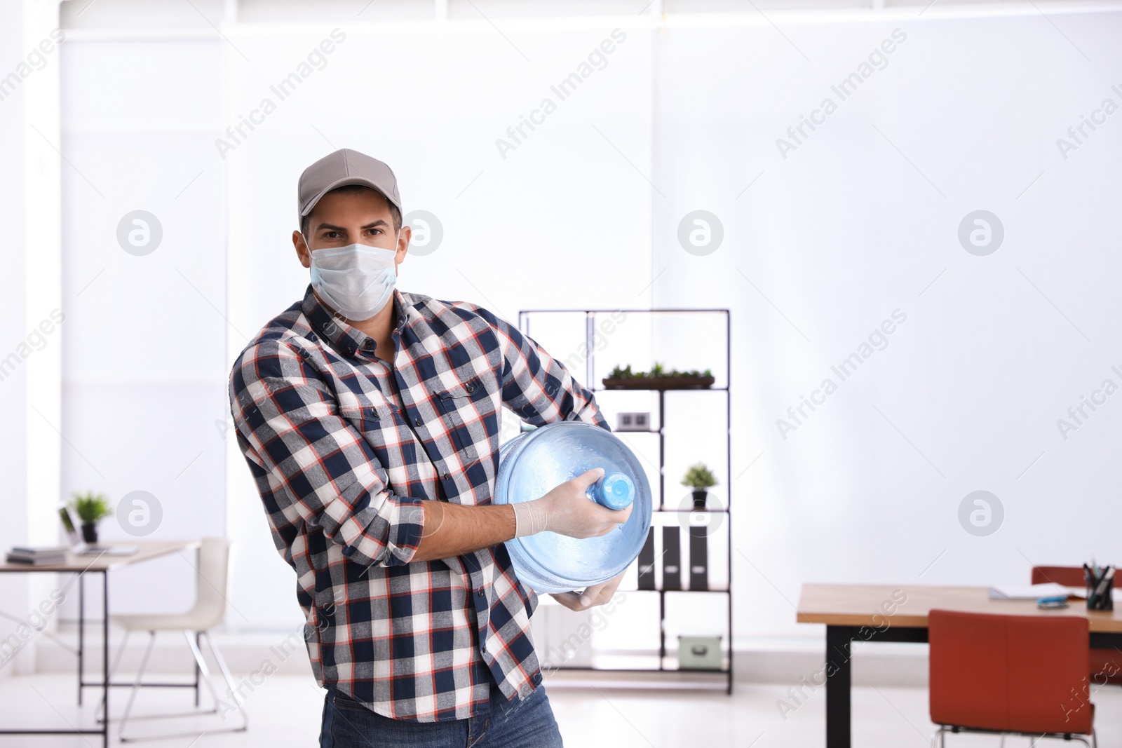 Photo of Courier in mask with bottle of cooler water indoors. Delivery during coronavirus quarantine