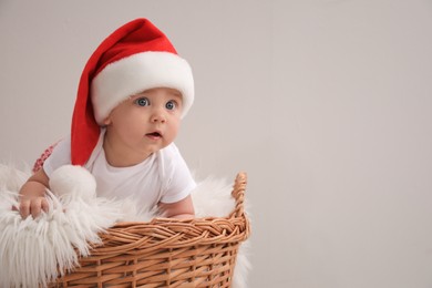 Photo of Cute baby in wicker basket on light grey background, space for text. Christmas celebration