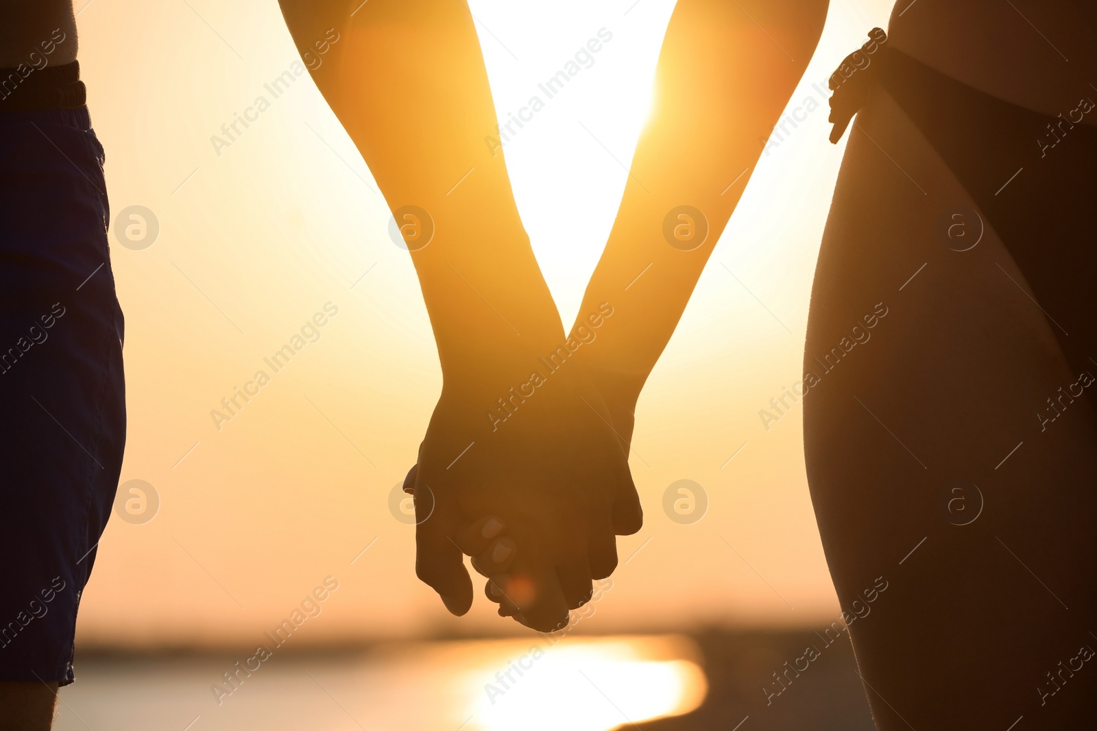 Photo of Woman in bikini holding hands with her boyfriend on beach at sunset, closeup. Lovely couple