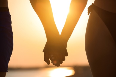 Woman in bikini holding hands with her boyfriend on beach at sunset, closeup. Lovely couple