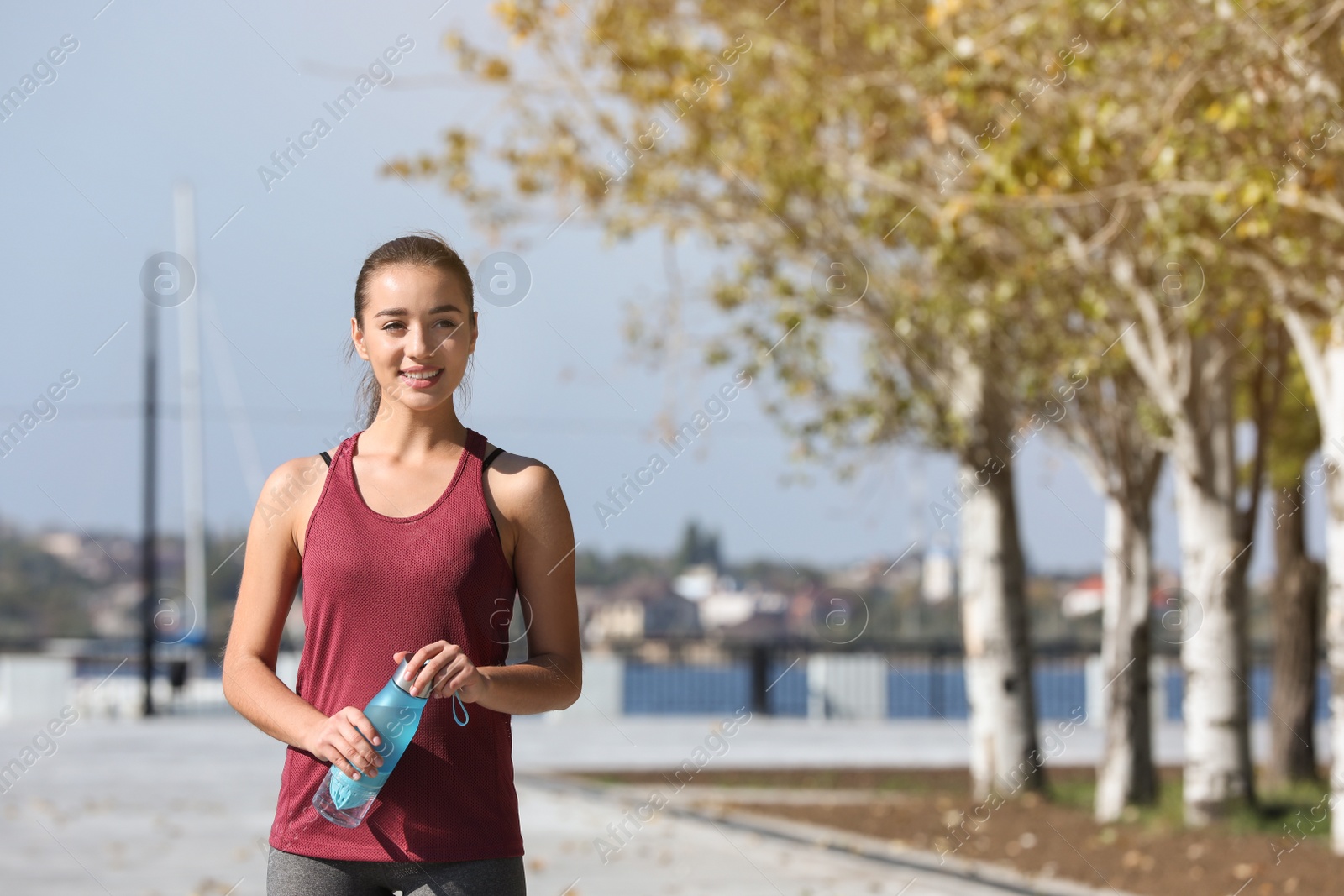 Photo of Young sporty woman holding bottle of water outdoors on sunny day. Space for text