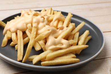 Photo of Delicious french fries with cheese sauce on wooden table, closeup