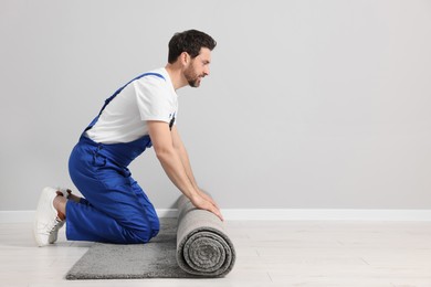 Worker unrolling new carpet on floor in room, space for text