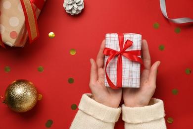 Woman holding Christmas gift on red background, top view