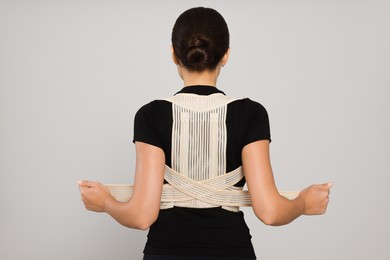 Woman with orthopedic corset on grey background, back view