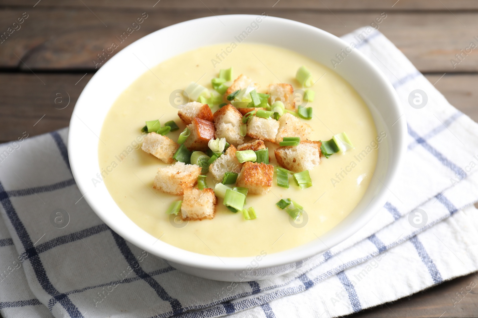 Photo of Tasty potato soup with croutons and green onion in bowl on table, closeup