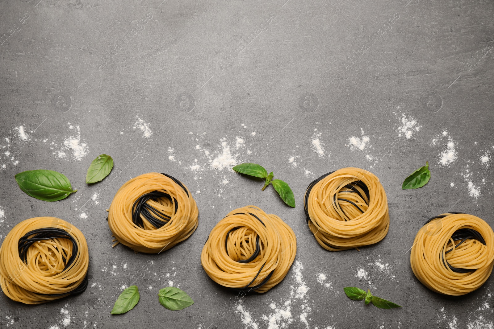 Photo of Raw linguine pasta with basil on grey table, flat lay. Space for text