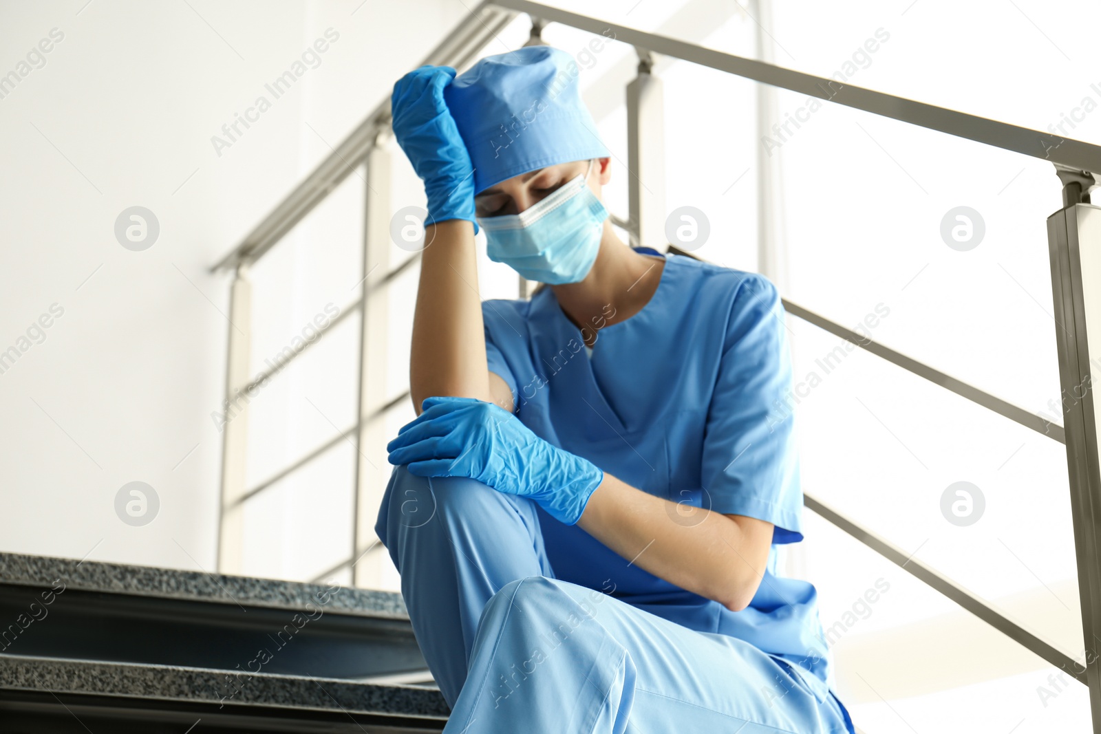 Photo of Exhausted doctor sitting on stairs in hospital. Stress of health care workers during COVID-19 pandemic