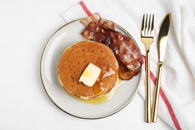 Delicious pancakes with maple syrup, butter and fried bacon on white wooden table, flat lay
