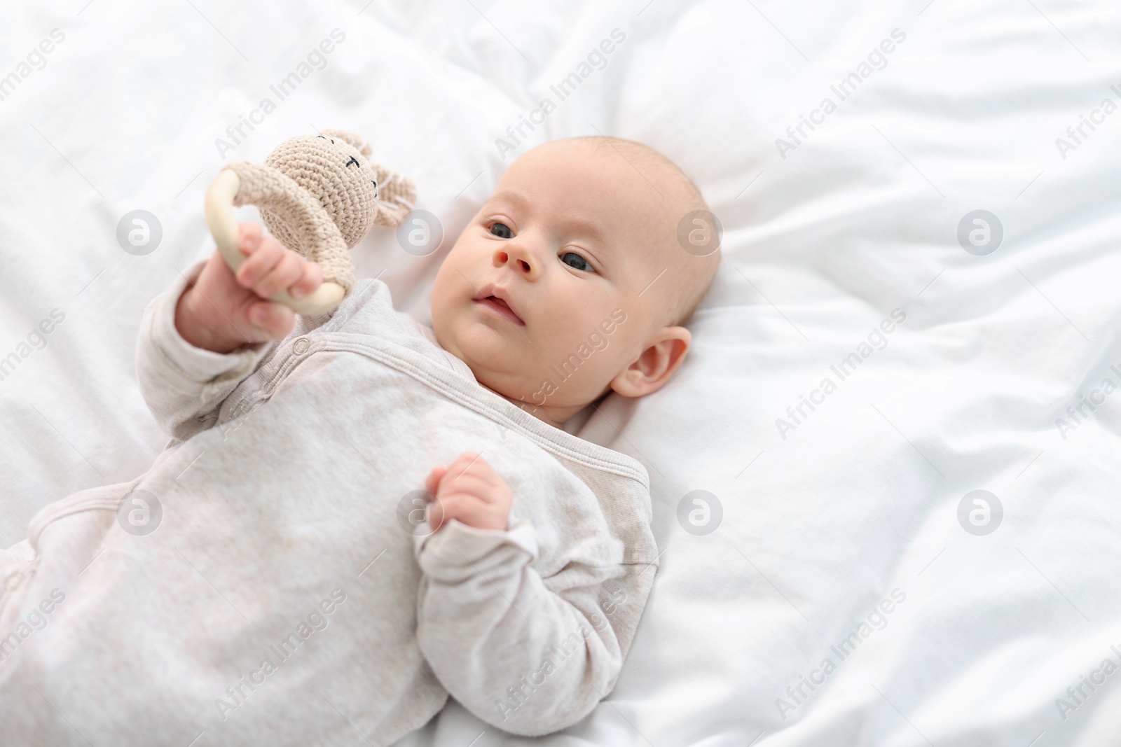 Photo of Cute little baby with toy lying on white sheets, space for text
