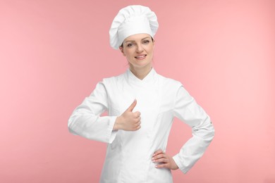 Photo of Happy woman chef in uniform showing thumbs up on pink background