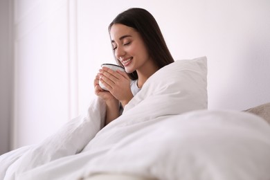 Woman covered in blanket holding cup of drink at home