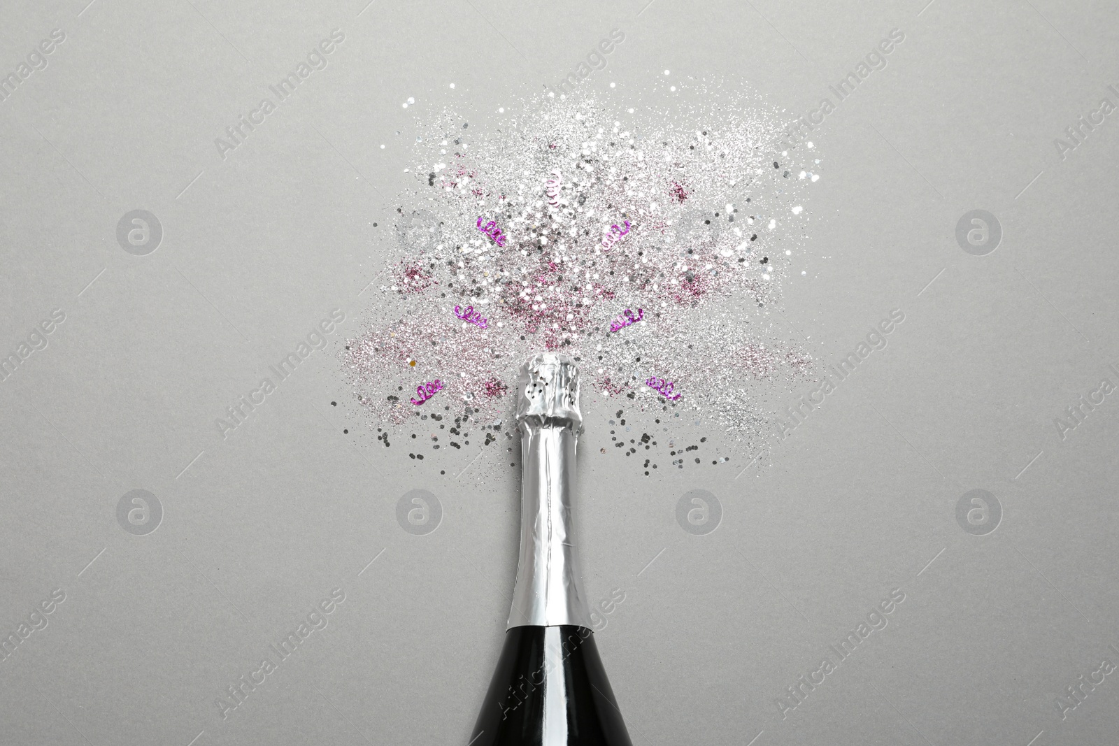 Photo of Bottle of champagne for celebration with glitter and confetti on grey background, top view