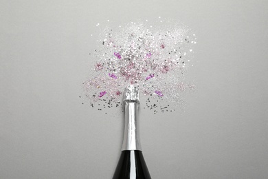 Bottle of champagne for celebration with glitter and confetti on grey background, top view