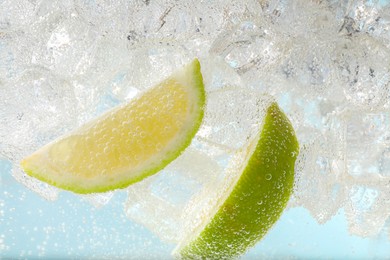 Juicy lime slices and ice cubes in soda water against light blue background, closeup