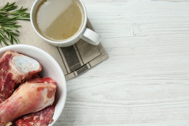 Photo of Mug with delicious bone broth and ingredients on white wooden table, flat lay. Space for text