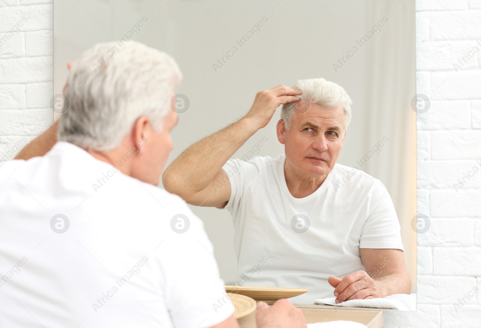 Photo of Senior man with hair loss problem looking in mirror indoors