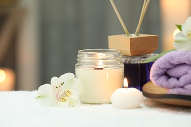 Beautiful composition with different spa products and flowers on white towel against blurred background, closeup. Space for text