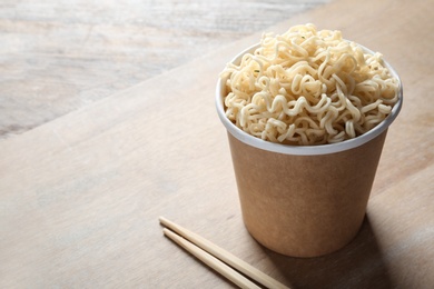 Photo of Paper cup of instant noodles and chopsticks on table. Space for text