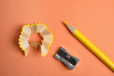 Photo of Color pencil, sharpener and shavings on orange background, flat lay