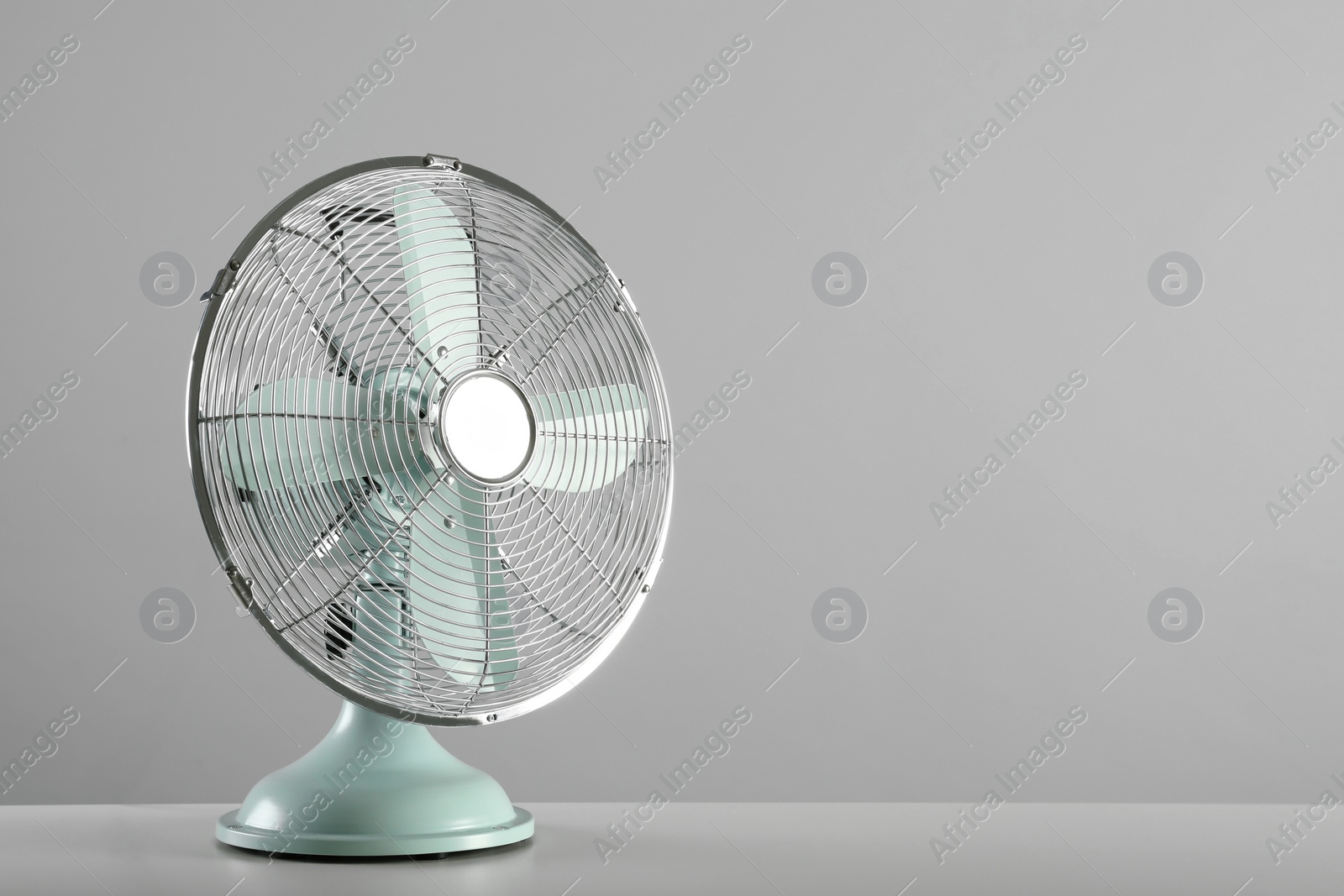 Photo of Electric fan on table against light grey background, space for text. Summer heat