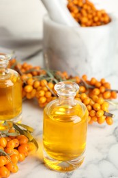 Photo of Natural sea buckthorn oil and fresh berries on white marble table